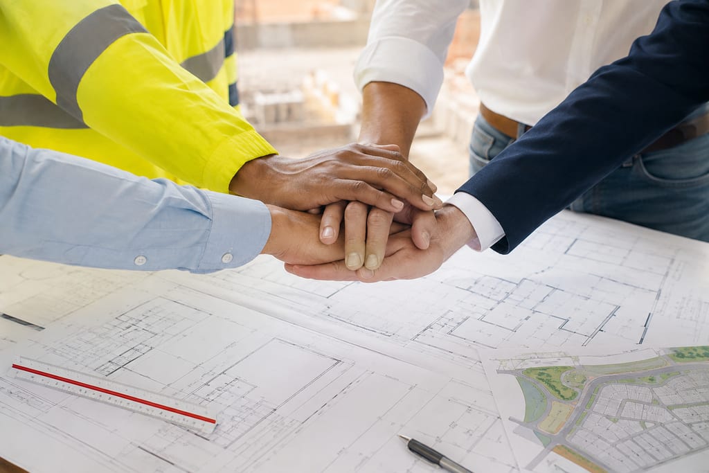 Manos del equipo de obra unidas sobre los planos de un proyecto